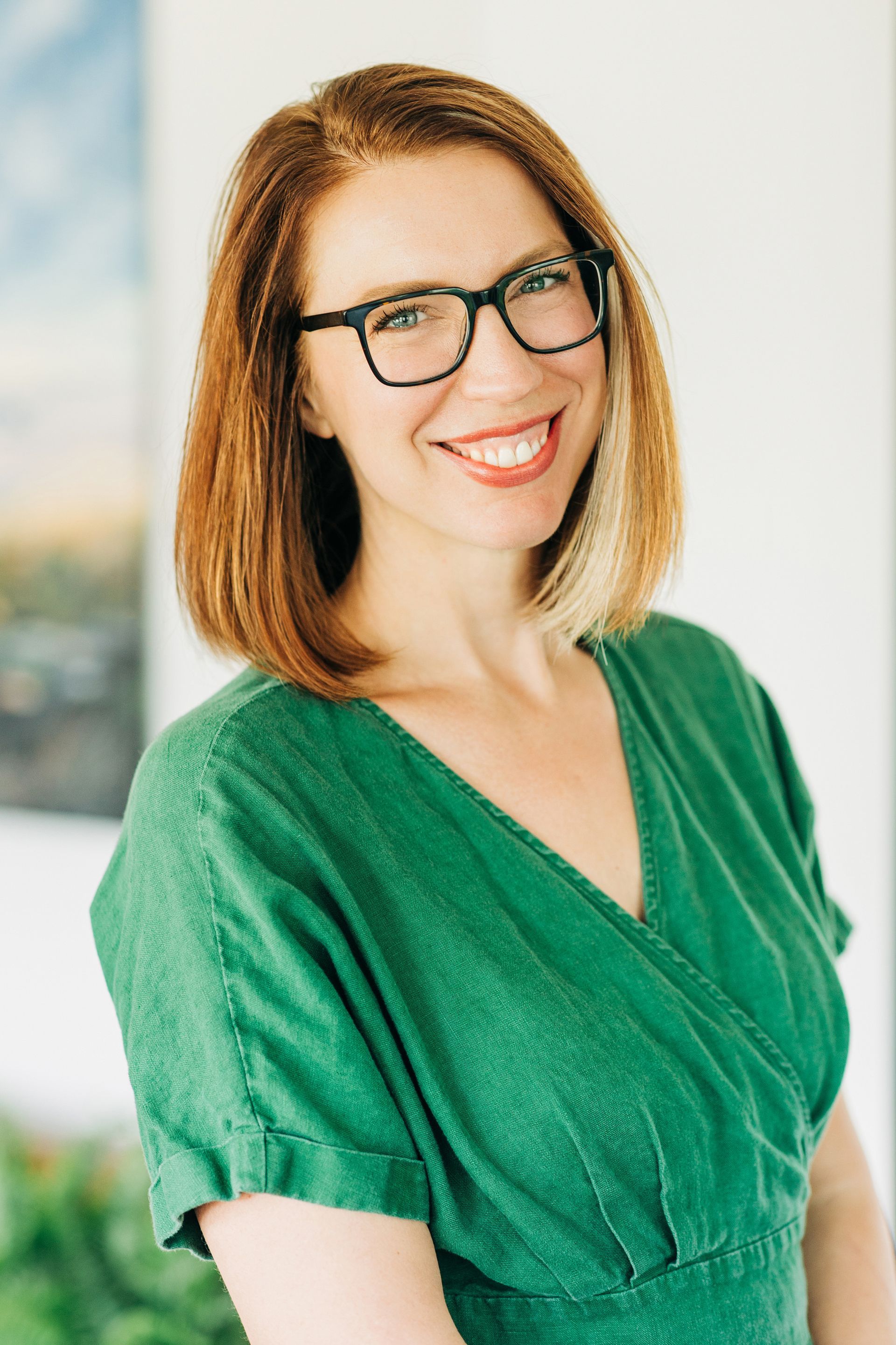 Woman in green dress and glasses smiles, outdoors.