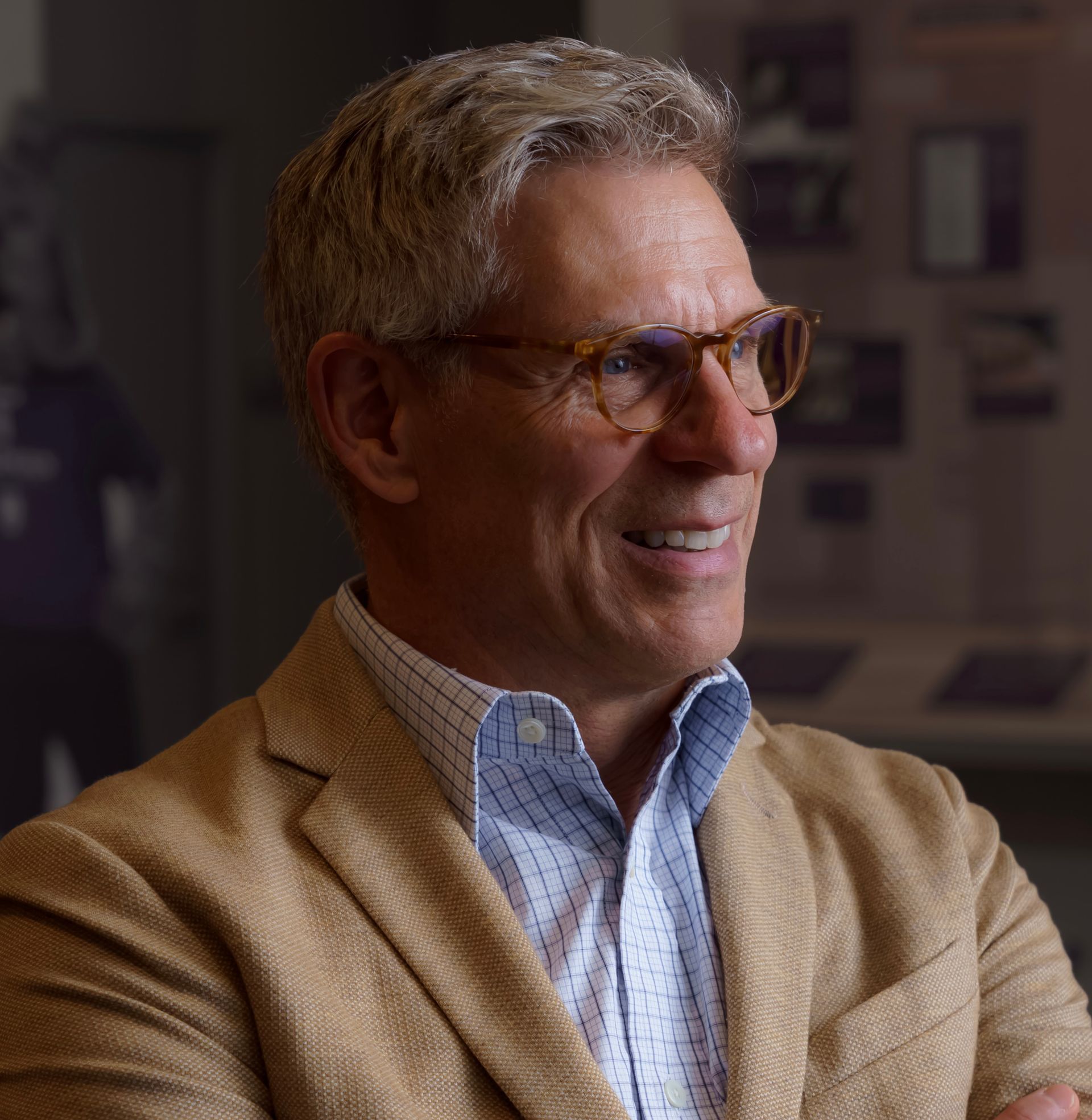 Man wearing glasses, light jacket, and button-down shirt, smiling in a room with displays.