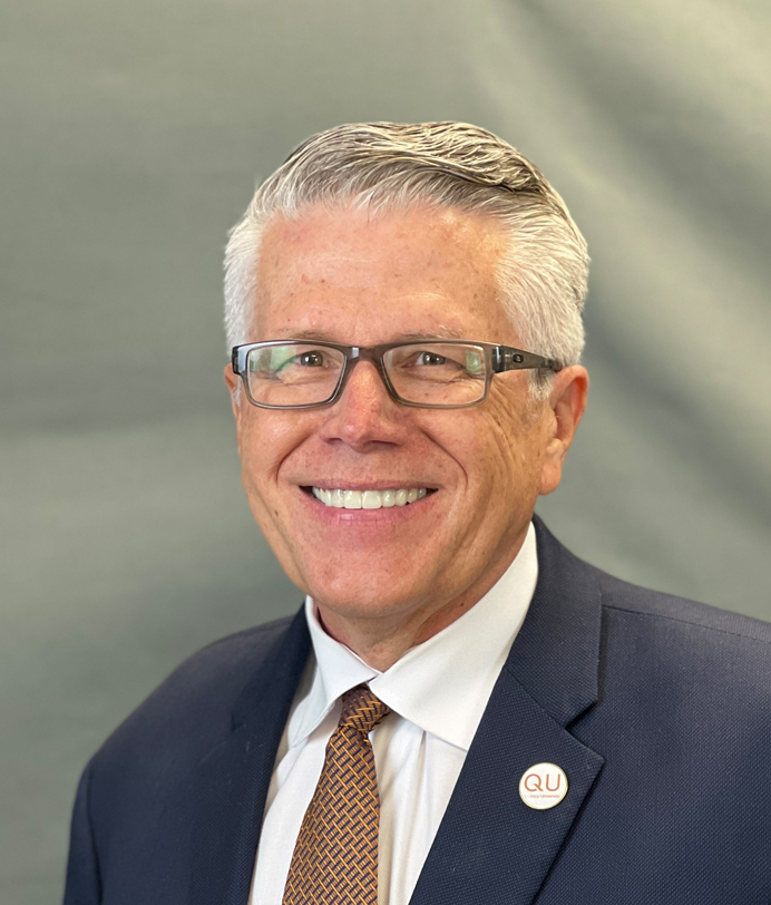 Man in suit smiling, wearing glasses.