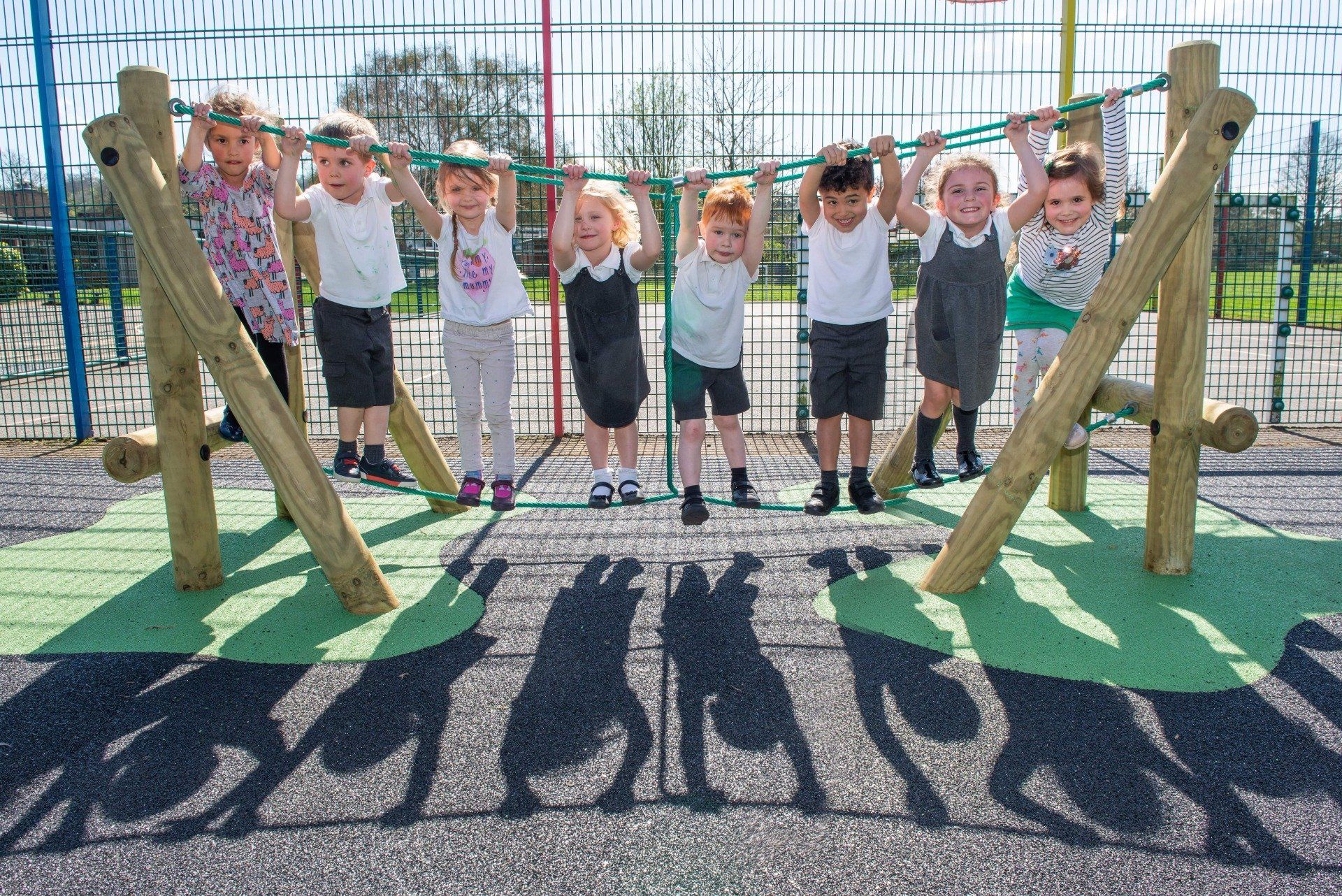 Children hanging from a playground structure on a sunny day; their shadows are visible.