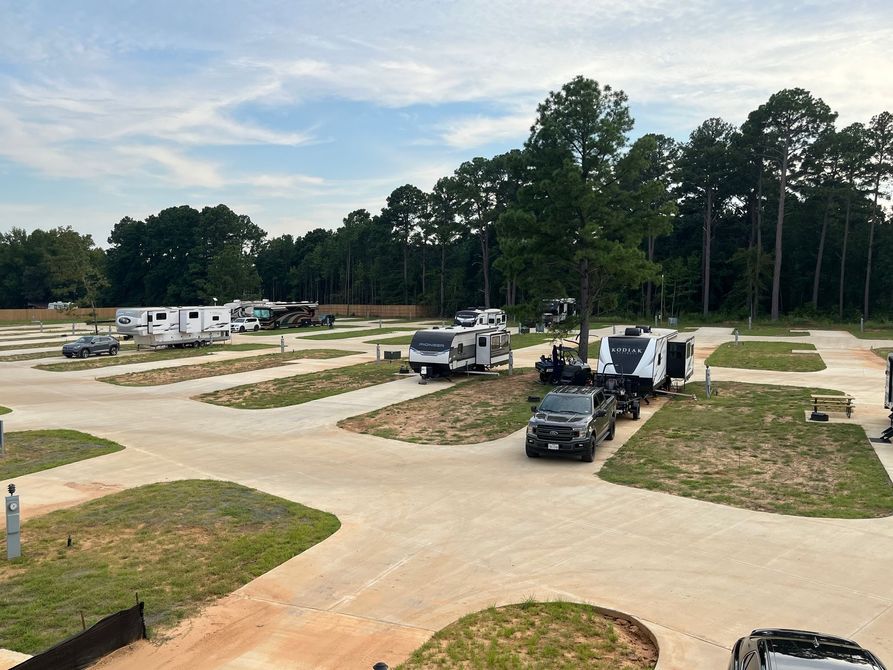 A lot of rvs are parked in a lot with trees in the background.