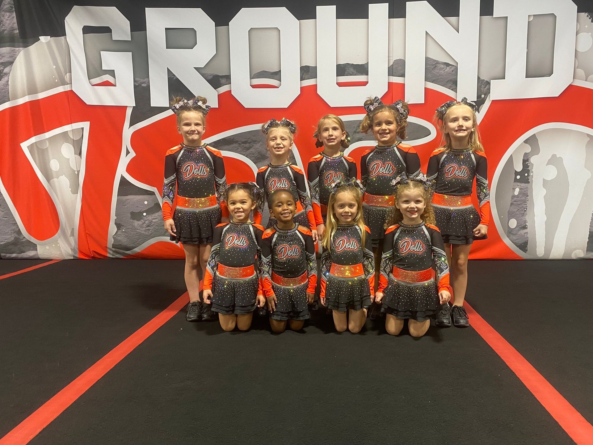 A group of cheerleaders are posing for a picture in front of a sign that says ground.