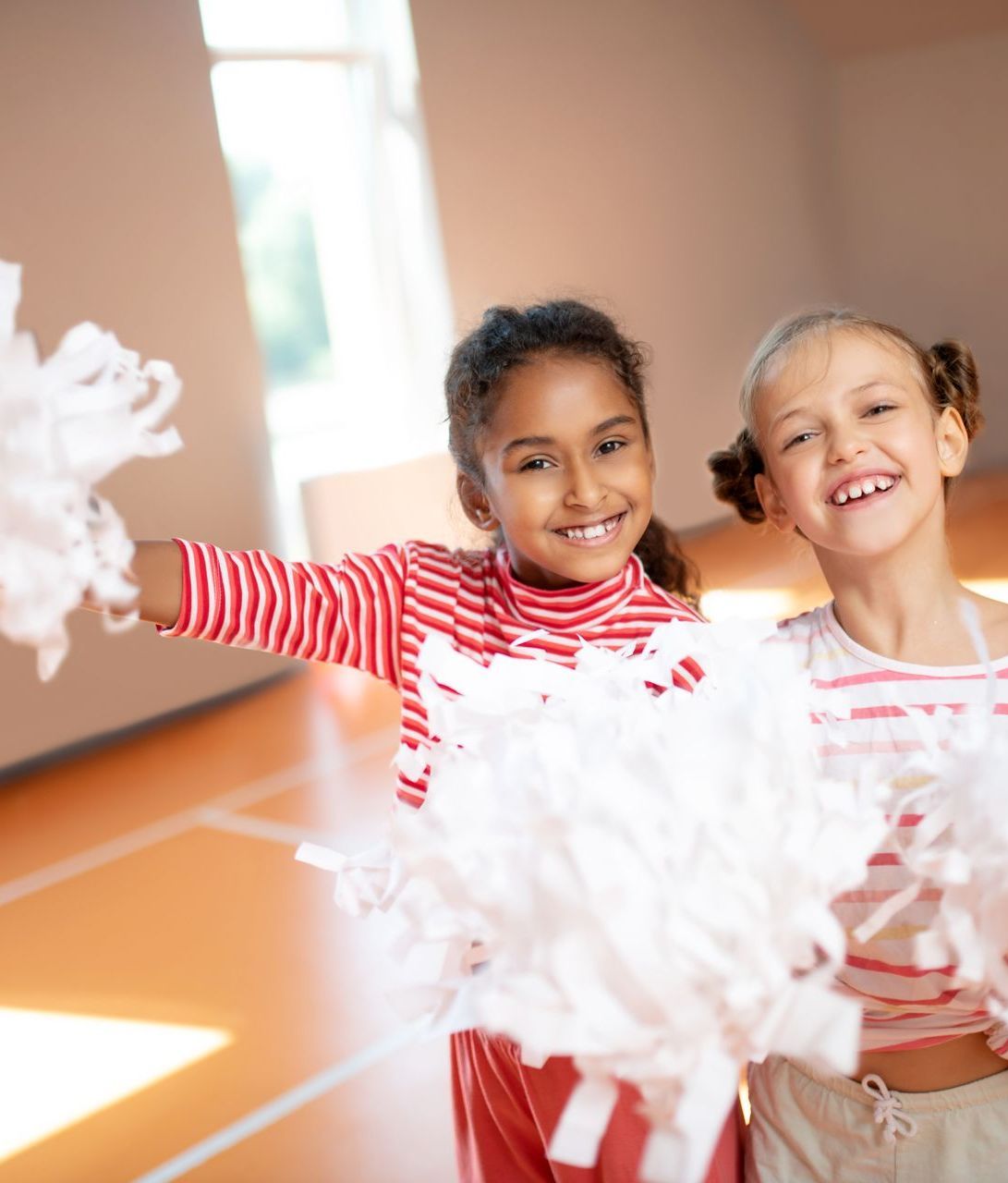 Two little girls are cheering with pom poms in a gym