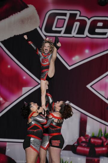 A cheerleader is being lifted in the air by two other cheerleaders.