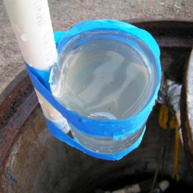 Plastic bottle with water taped to a pipe, inside a dark, open container.