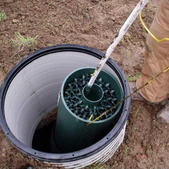 A septic system component is being lowered into an open concrete well, with a person nearby.