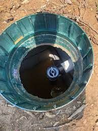 Open green septic tank access in dirt, showing dark water and internal components.