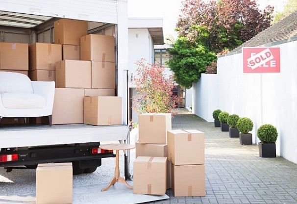 A moving truck filled with boxes and a sold sign in the background