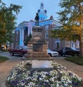 A statue of a man standing on top of a stone pedestal in front of a building.