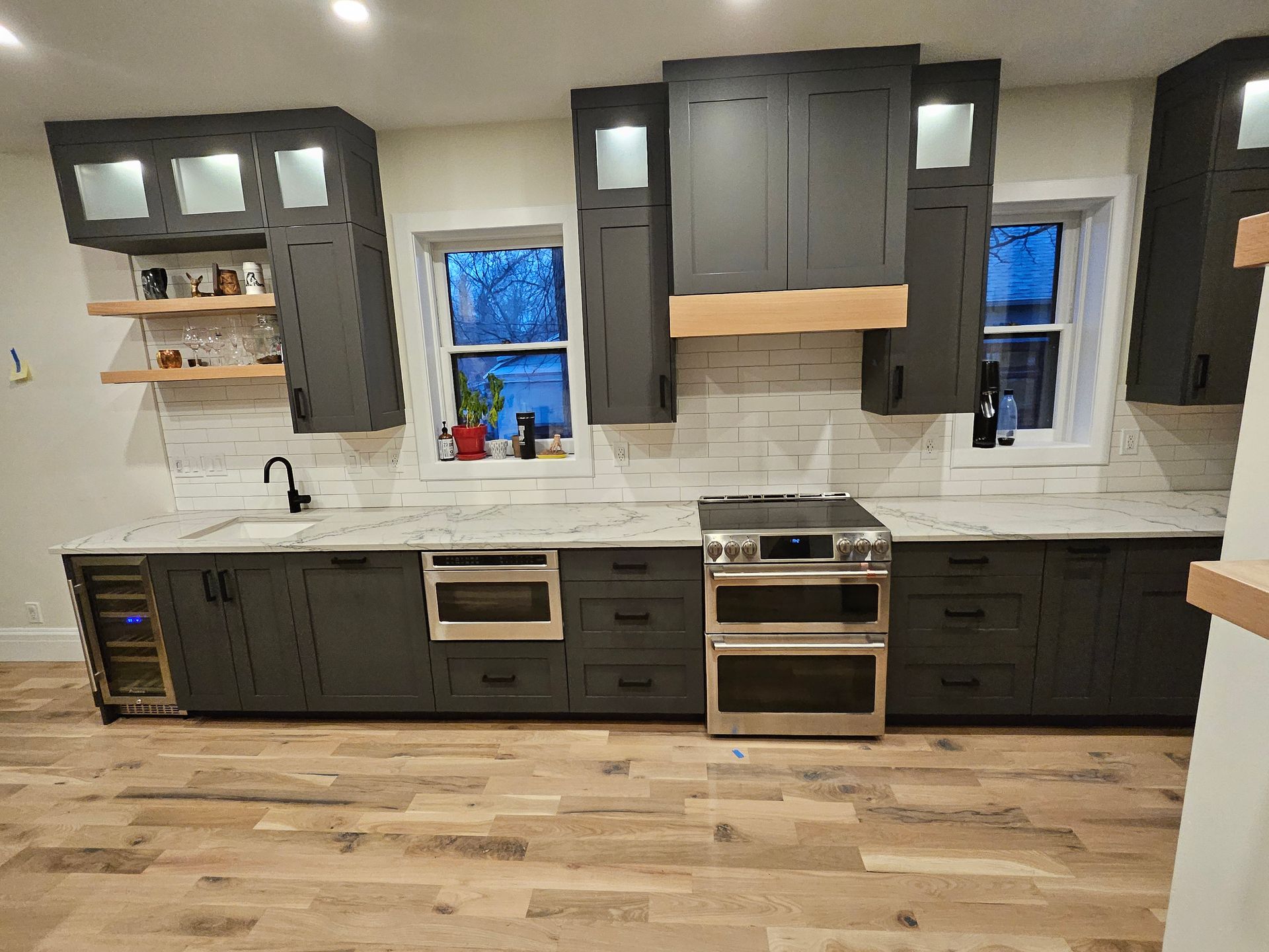 A kitchen with gray cabinets , white counter tops , stainless steel appliances and a wine cooler.