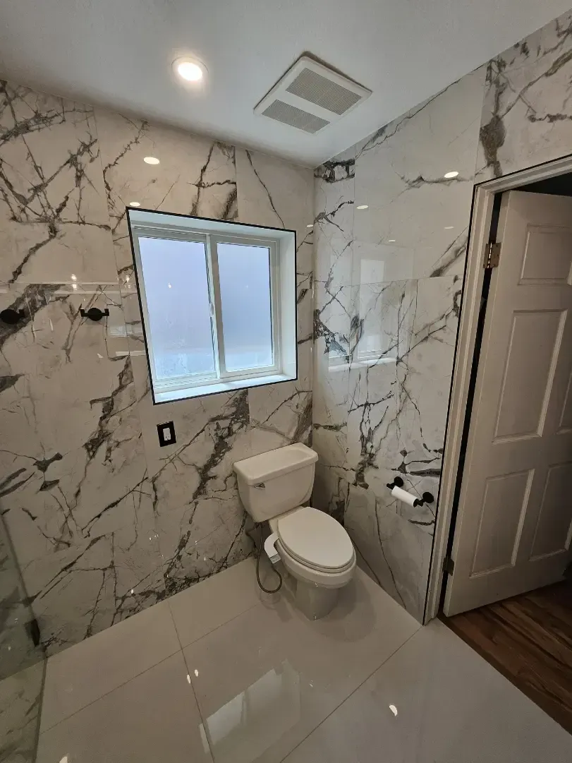 A bathroom with marble walls and a toilet and a window