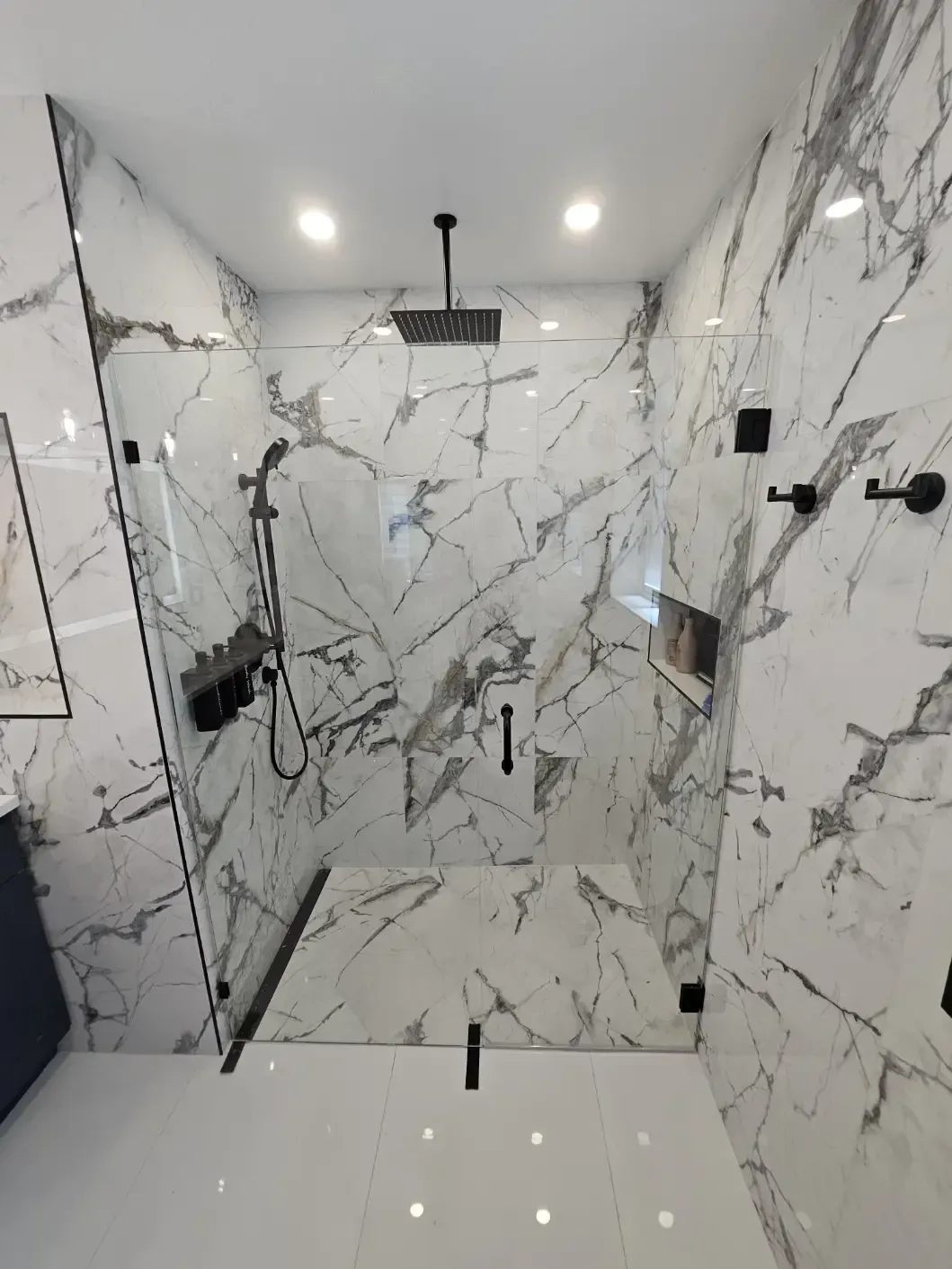 A bathroom with marble walls and a walk in shower with a glass door.