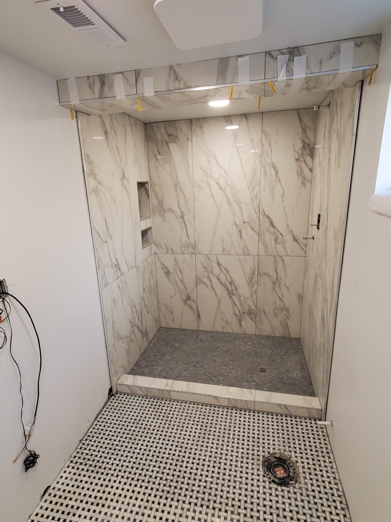 A bathroom with a marble shower and a black and white tile floor.