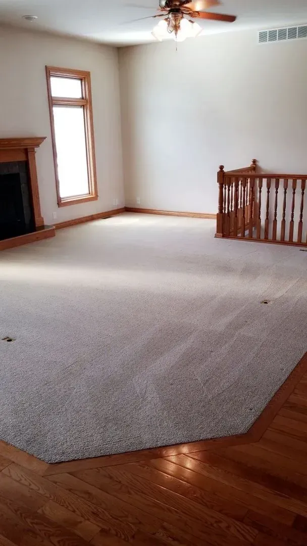 An empty living room with hardwood floors , a fireplace and a ceiling fan.
