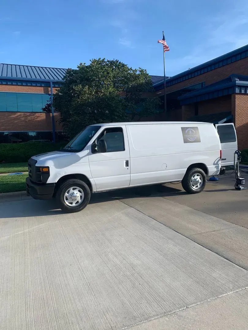 A white van is parked in a parking lot in front of a building.