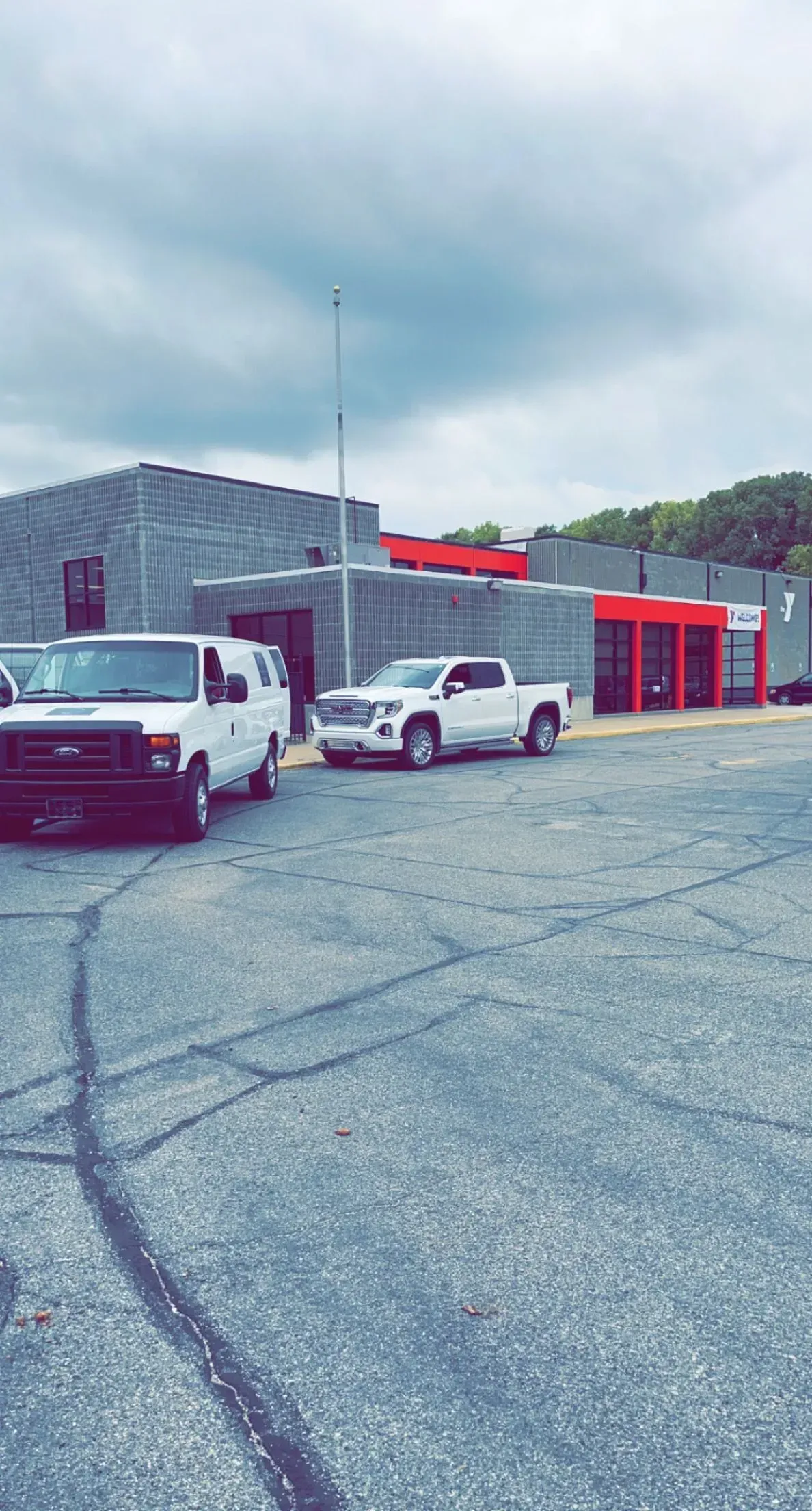 Two white trucks are parked in a parking lot in front of a building.