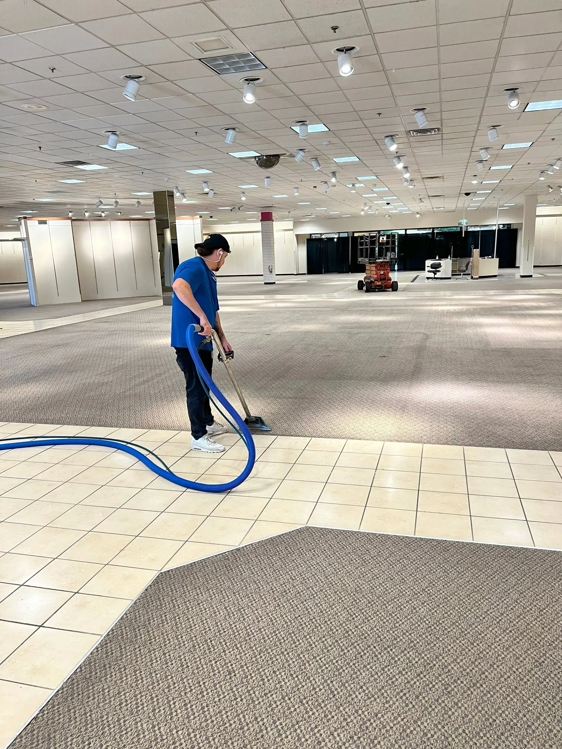 A woman is cleaning a large room with a vacuum cleaner.