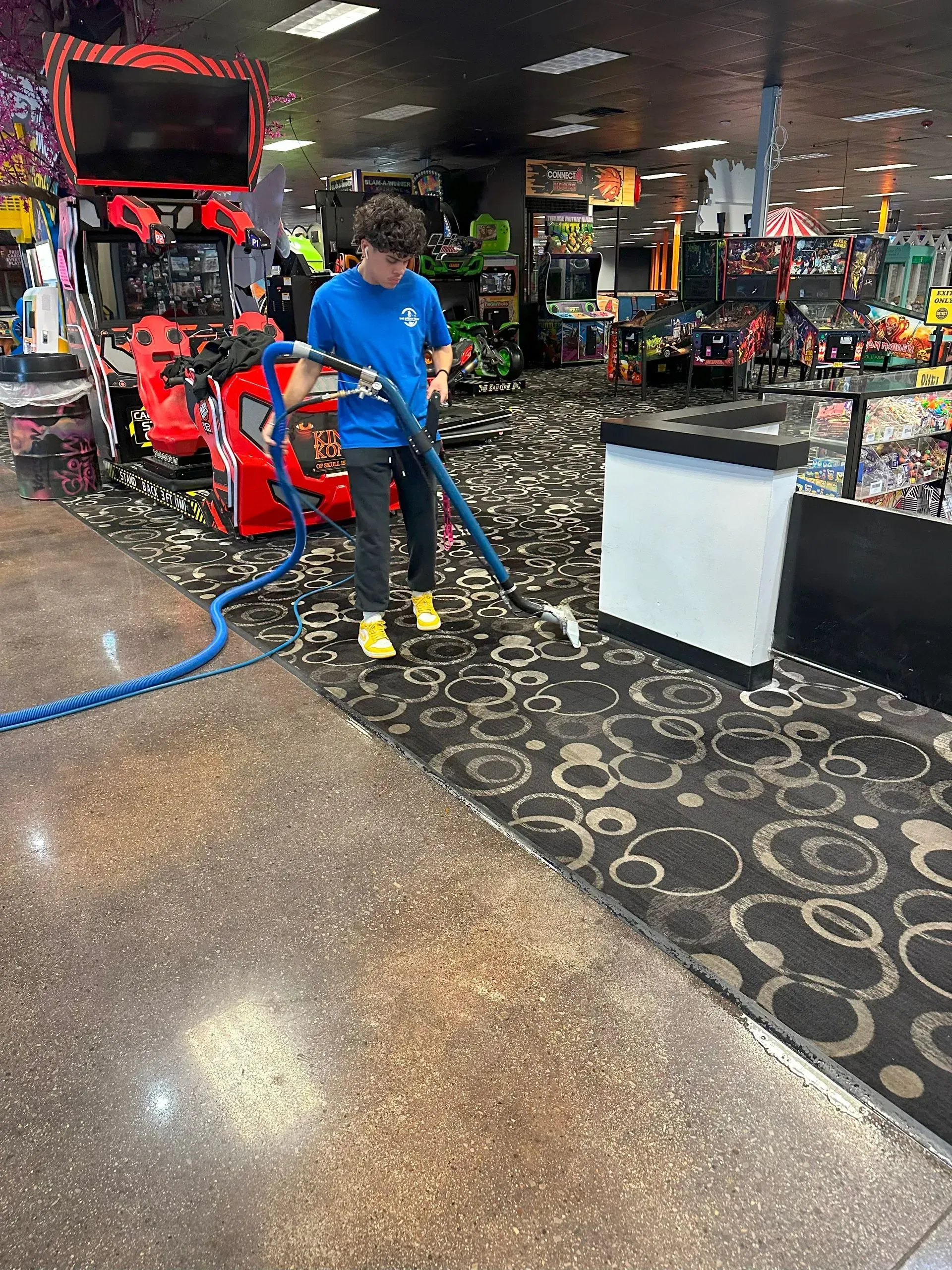 A man is cleaning the floor of an arcade with a vacuum cleaner.