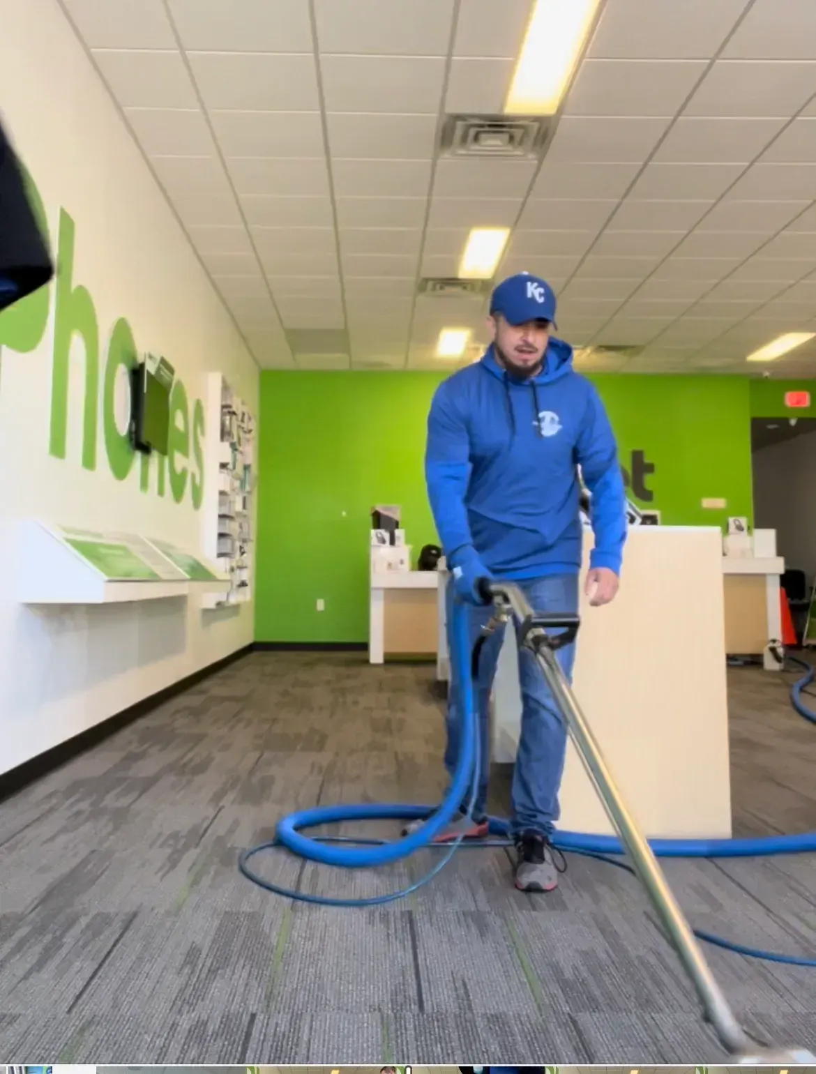 A man in a blue hoodie is using a vacuum cleaner in an office