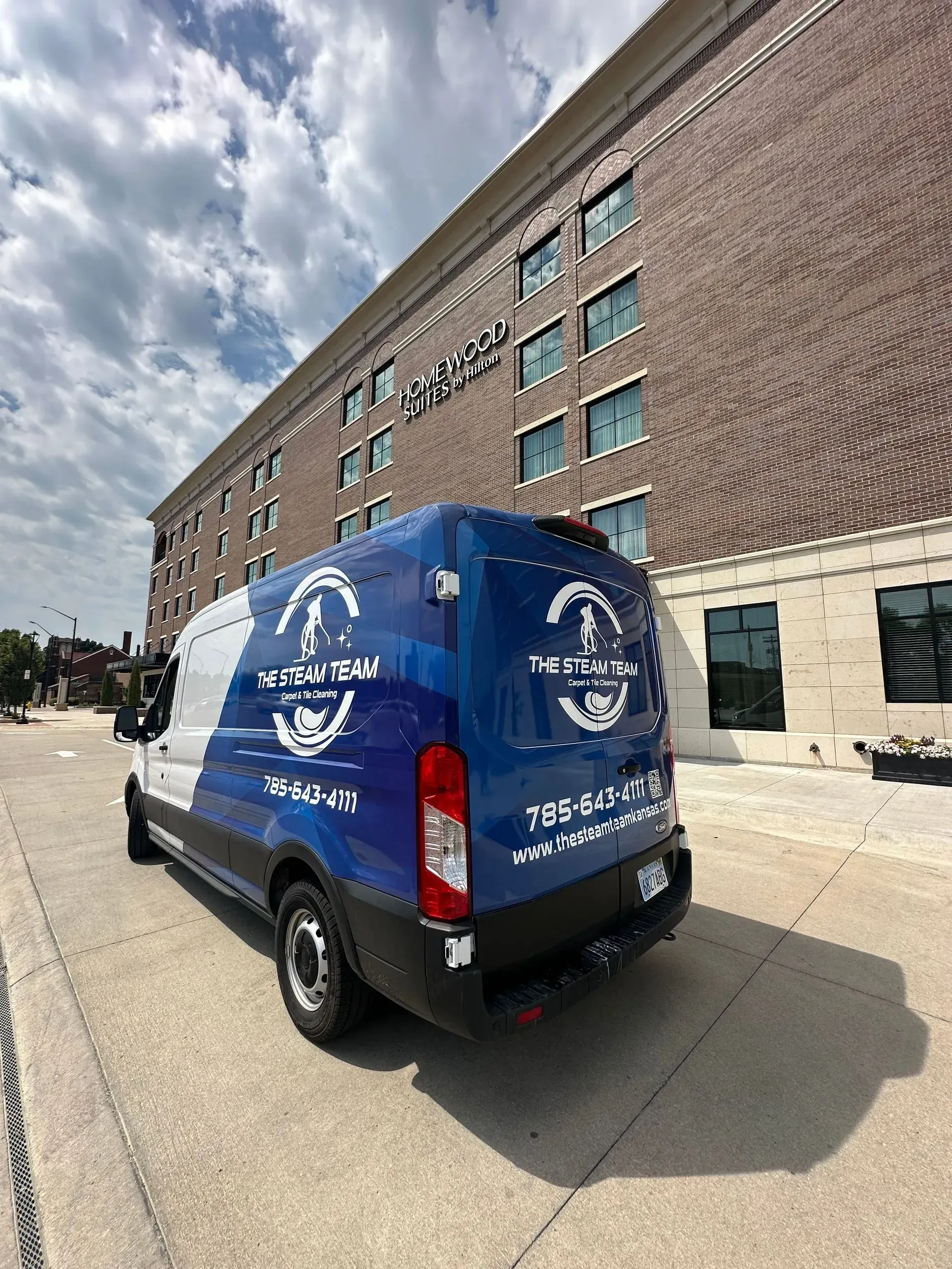 A blue and white van is parked in front of a brick building.