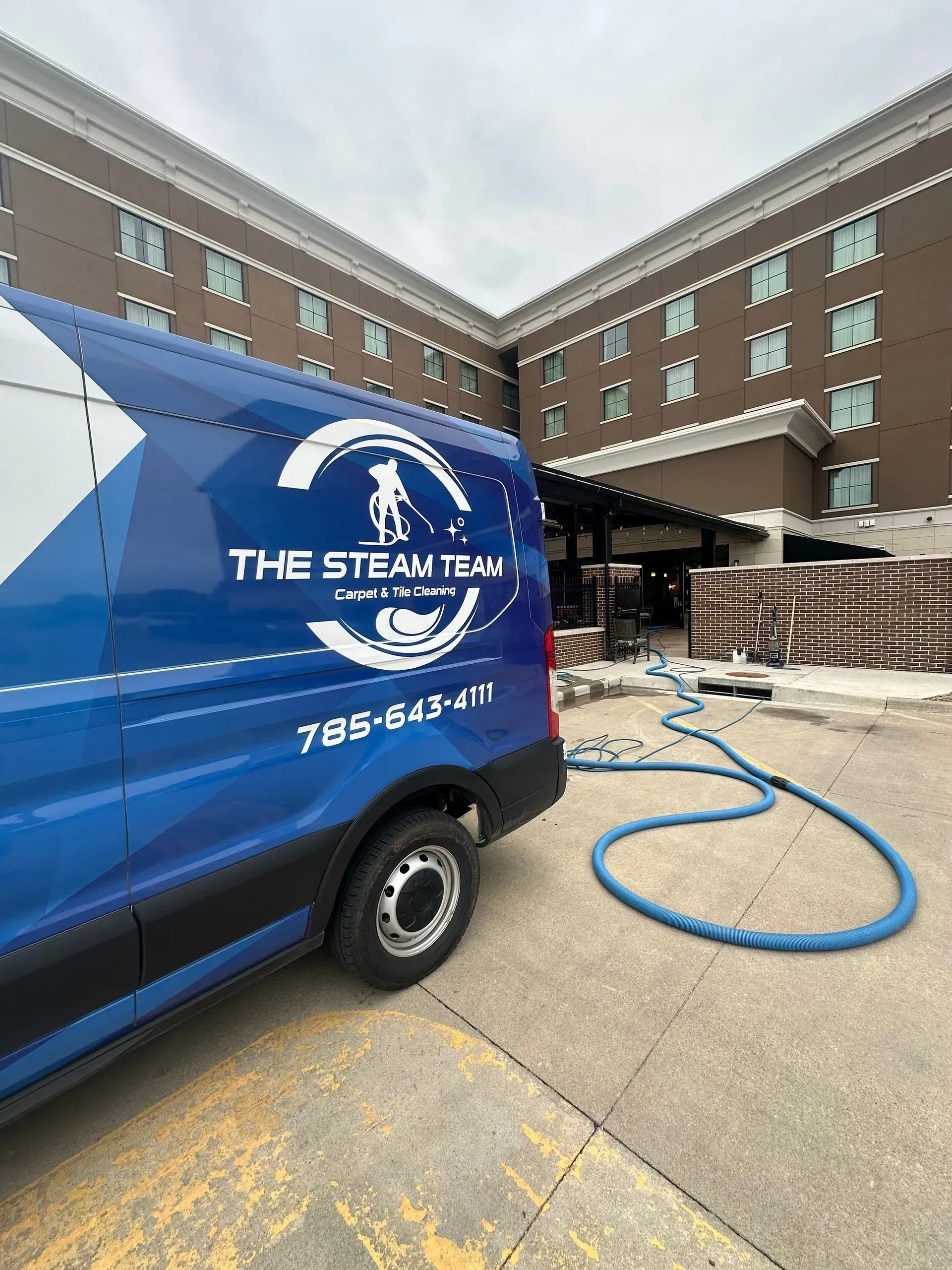 A blue van is parked in front of a large building.