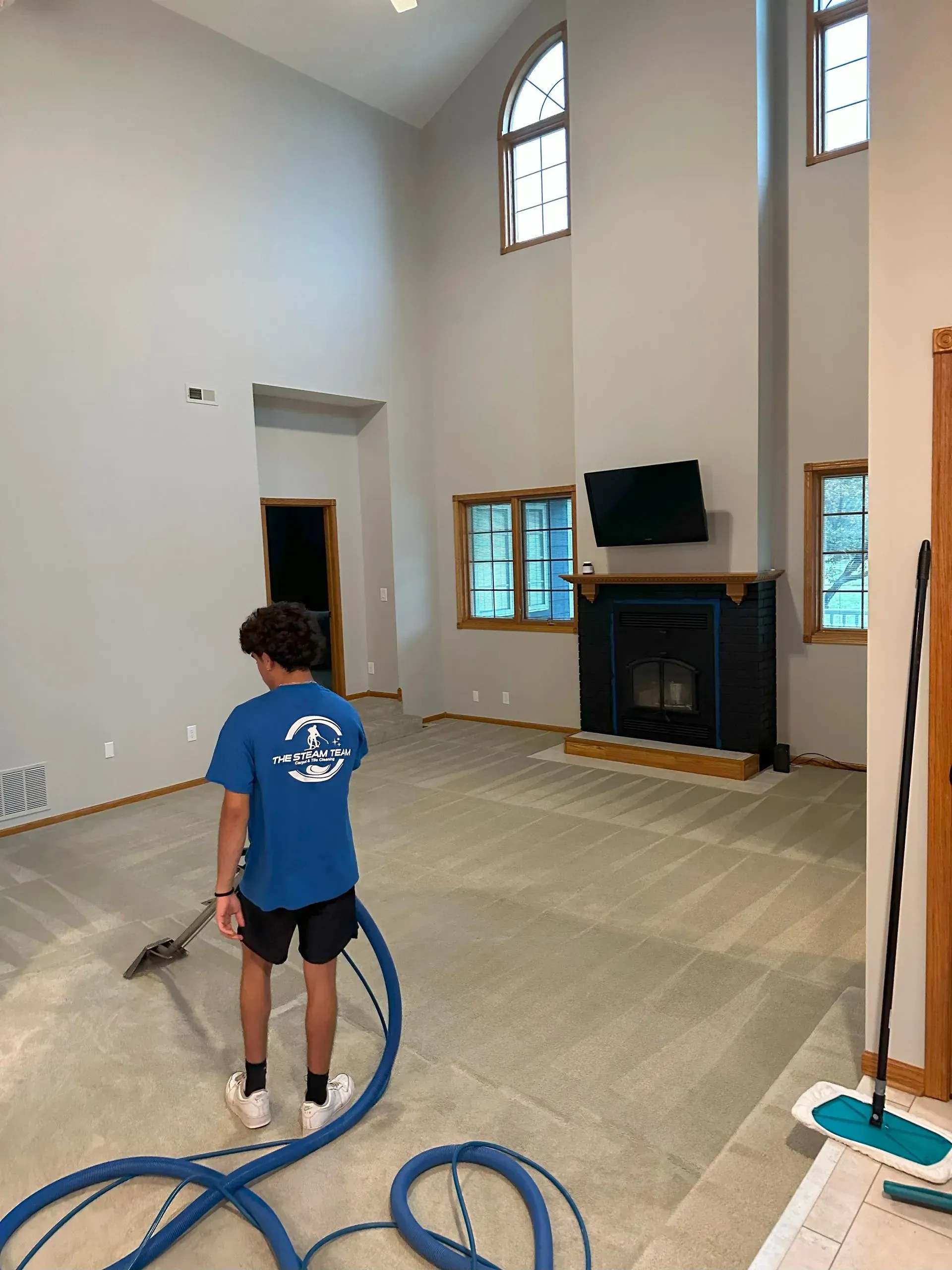 A boy in a blue shirt is cleaning the floor of a living room with a vacuum cleaner.