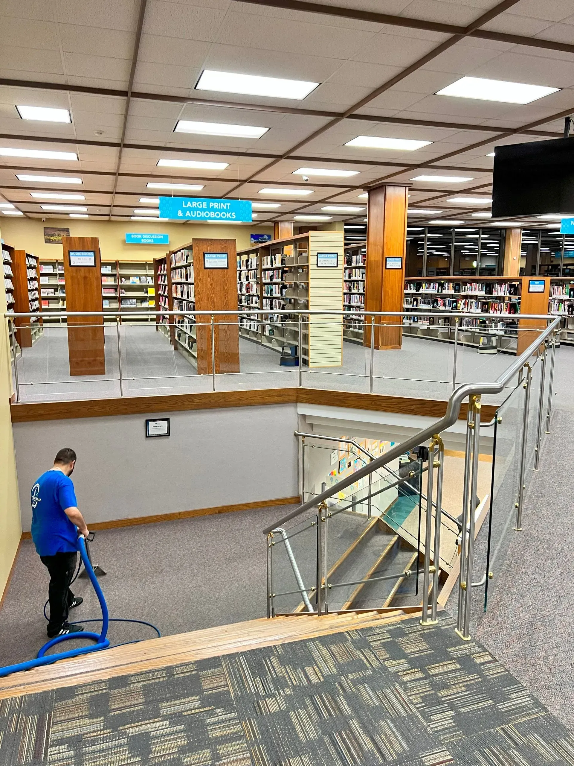 A man is cleaning the floor of a library with a vacuum cleaner.