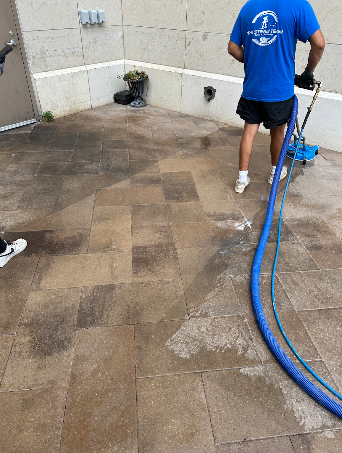 A man in a blue shirt is cleaning a brick floor with a hose
