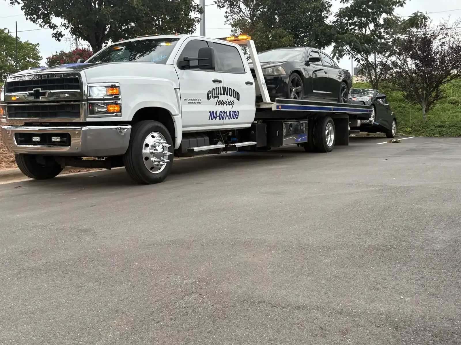 Tow truck carrying a car on a flatbed; white truck with 