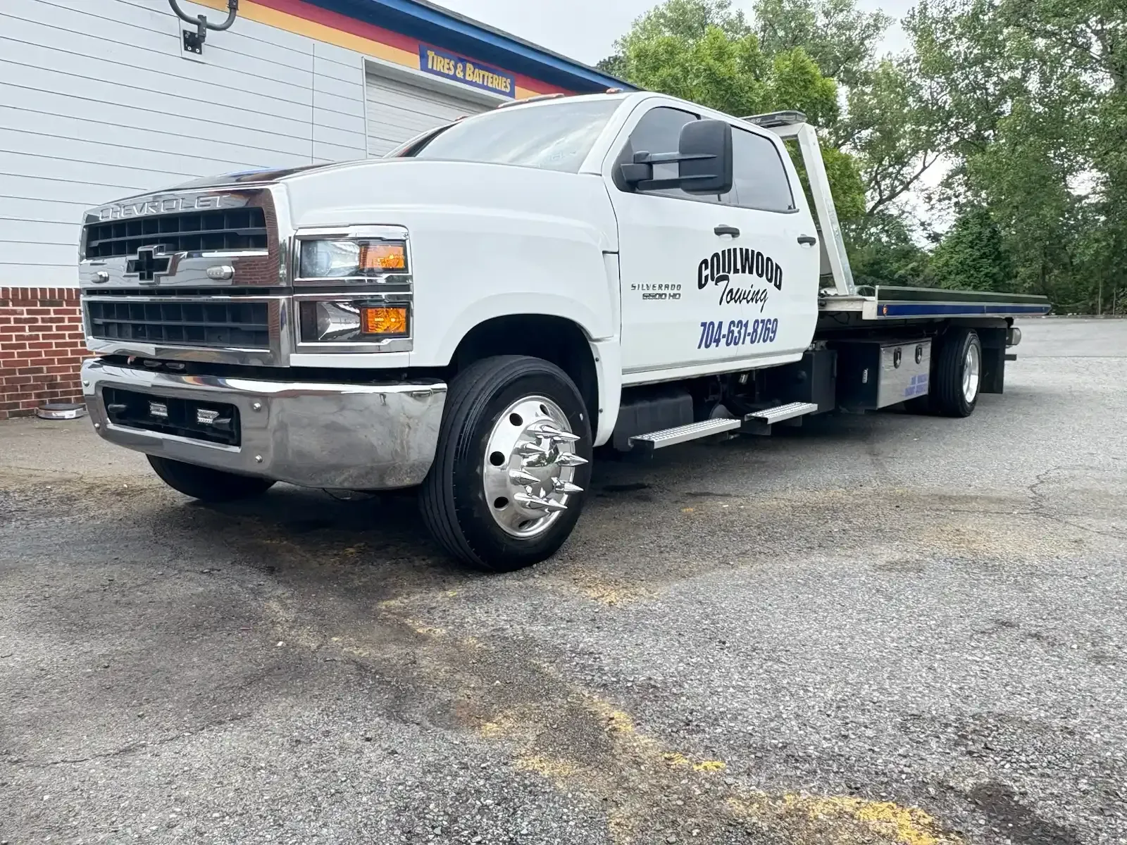 White tow truck parked in front of a building; company name on the door.