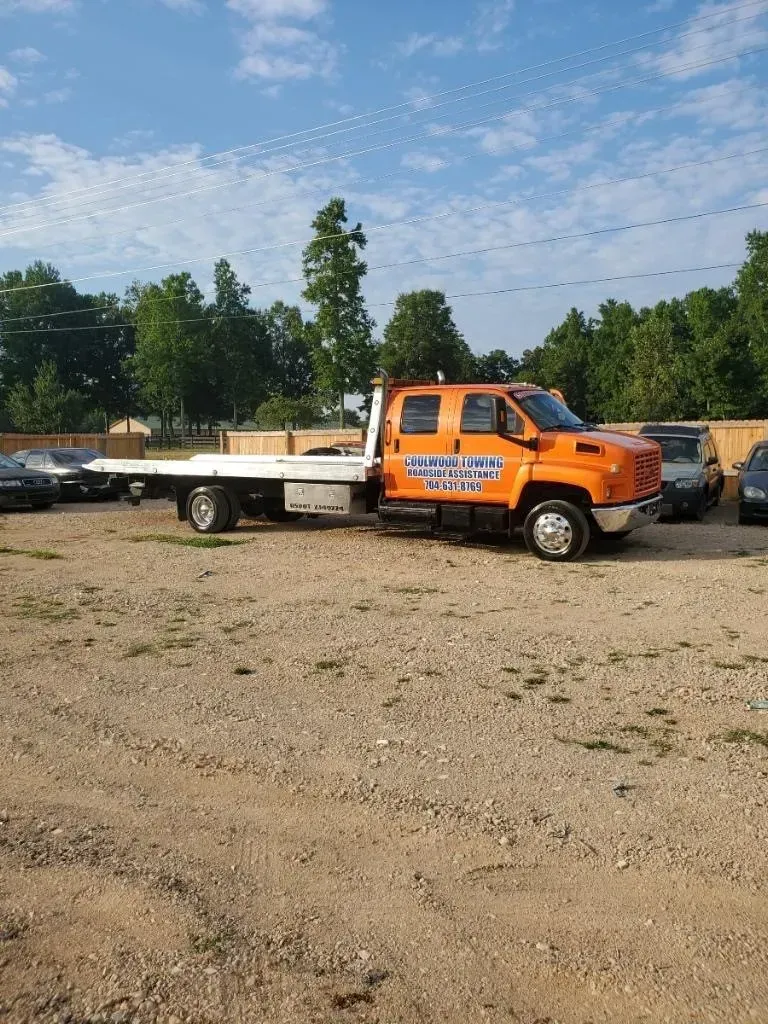 Orange tow truck on a gravel lot under a partly cloudy blue sky.
