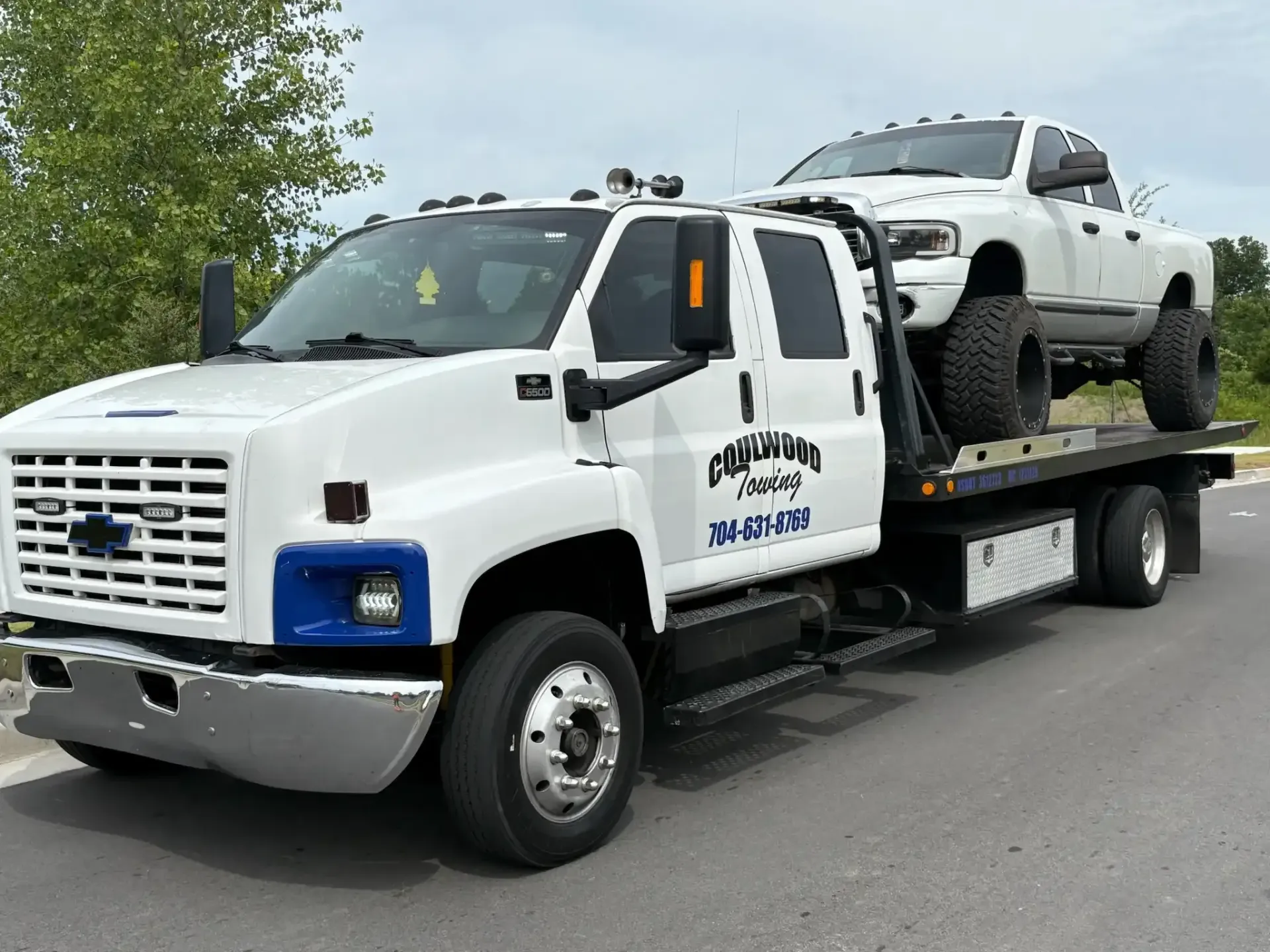 White tow truck carrying a white pickup truck on a paved road. 