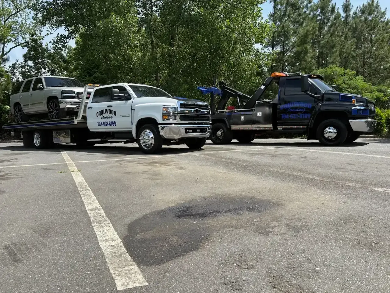 Two tow trucks in a parking lot, one carrying a silver SUV.