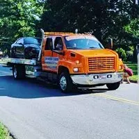 Orange tow truck carrying a black car on a road.