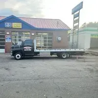 Black flatbed tow truck parked near a building with garage bays.