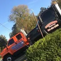 Orange tow truck partially obscured by bushes beside a black tow truck.