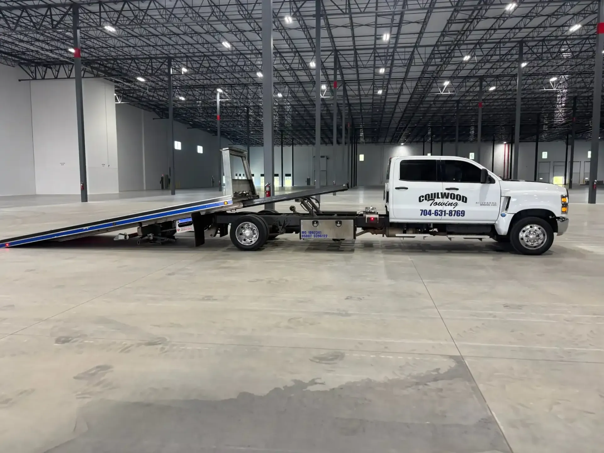 White tow truck with flatbed in a large, empty warehouse.