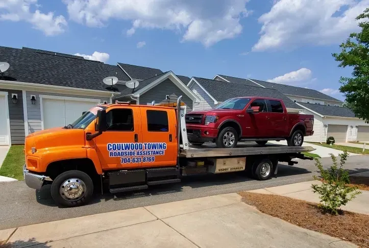 Orange tow truck carrying a red pickup truck in a residential area.