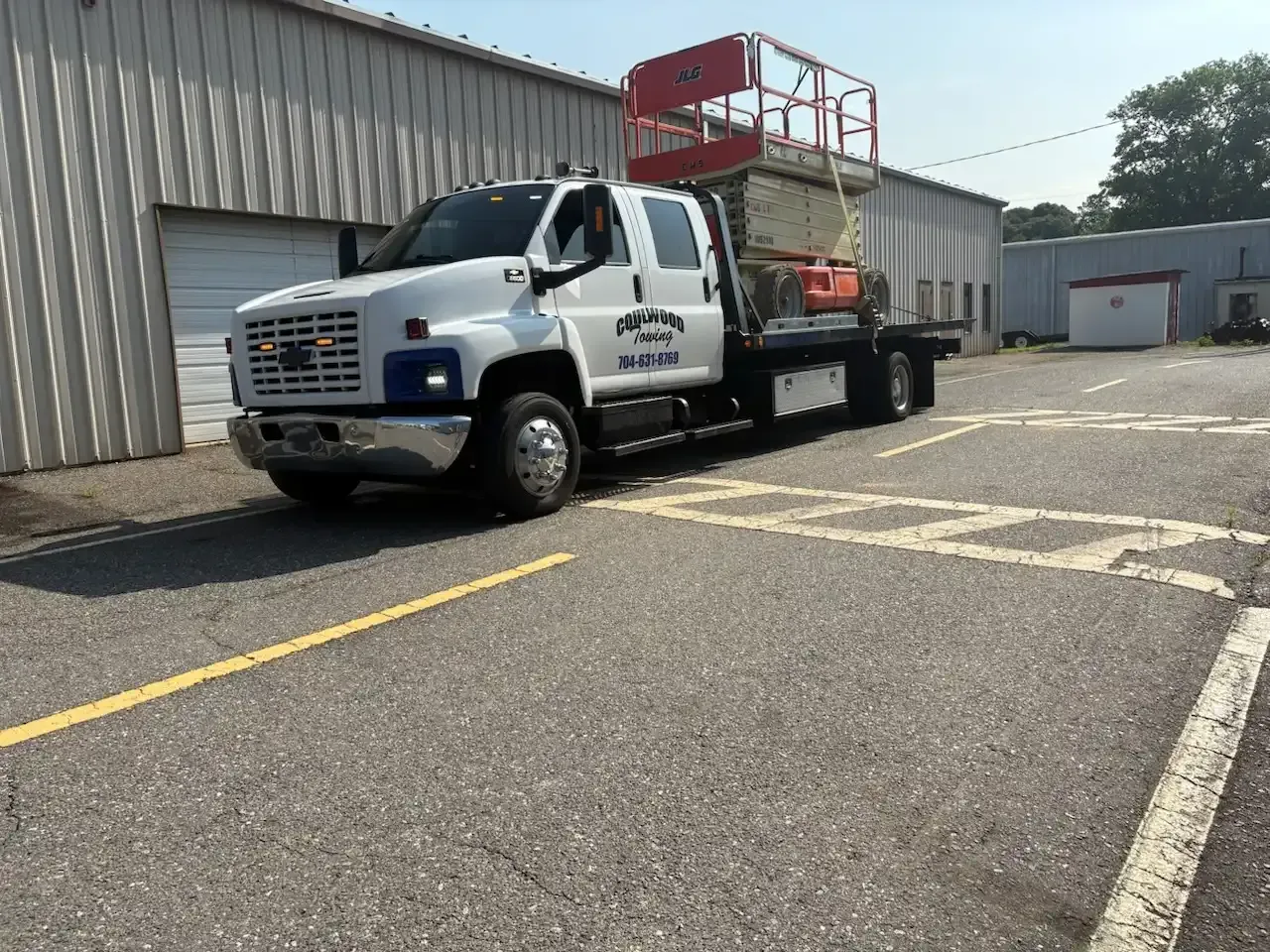 White truck with a lift on the flatbed, parked in a lot in front of a building.