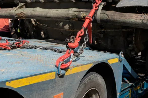 A truck bed with heavy chains and red hooks securing a large, cylindrical object.