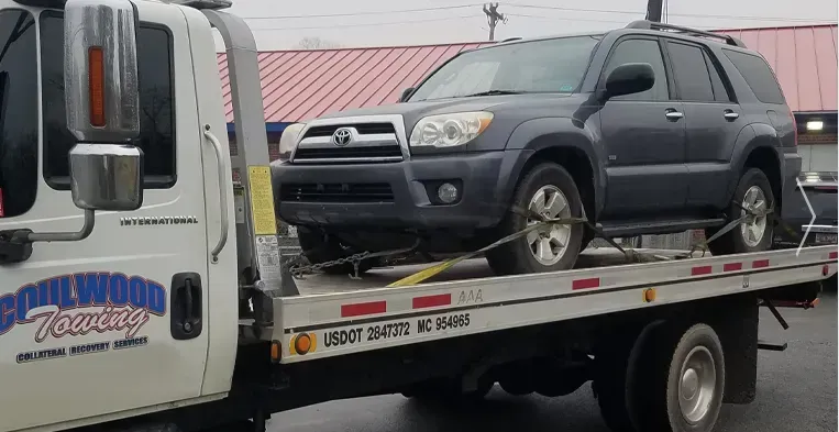 A dark blue SUV is being towed on a flatbed tow truck by Coolwood Towing.