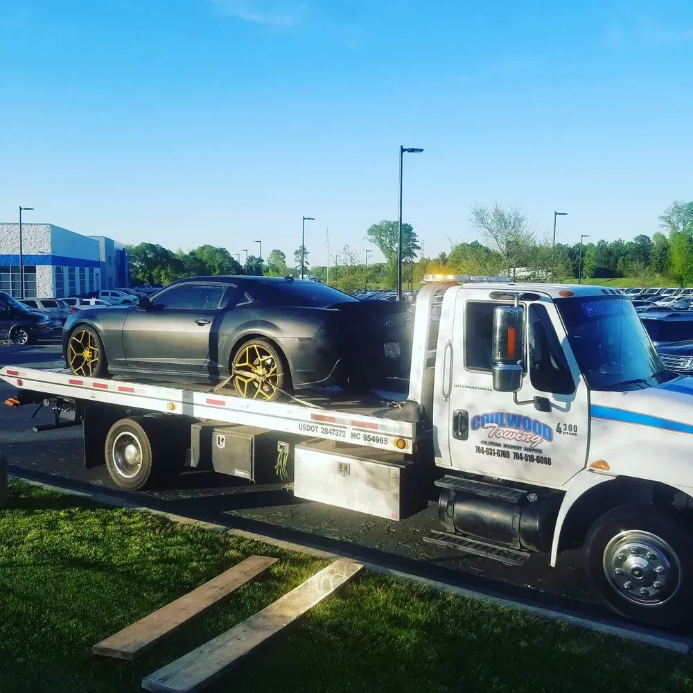 A black sports car is towed on a flatbed tow truck outdoors on a sunny day.