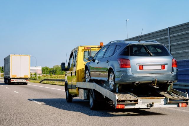 Yellow tow truck towing a silver car on a highway.