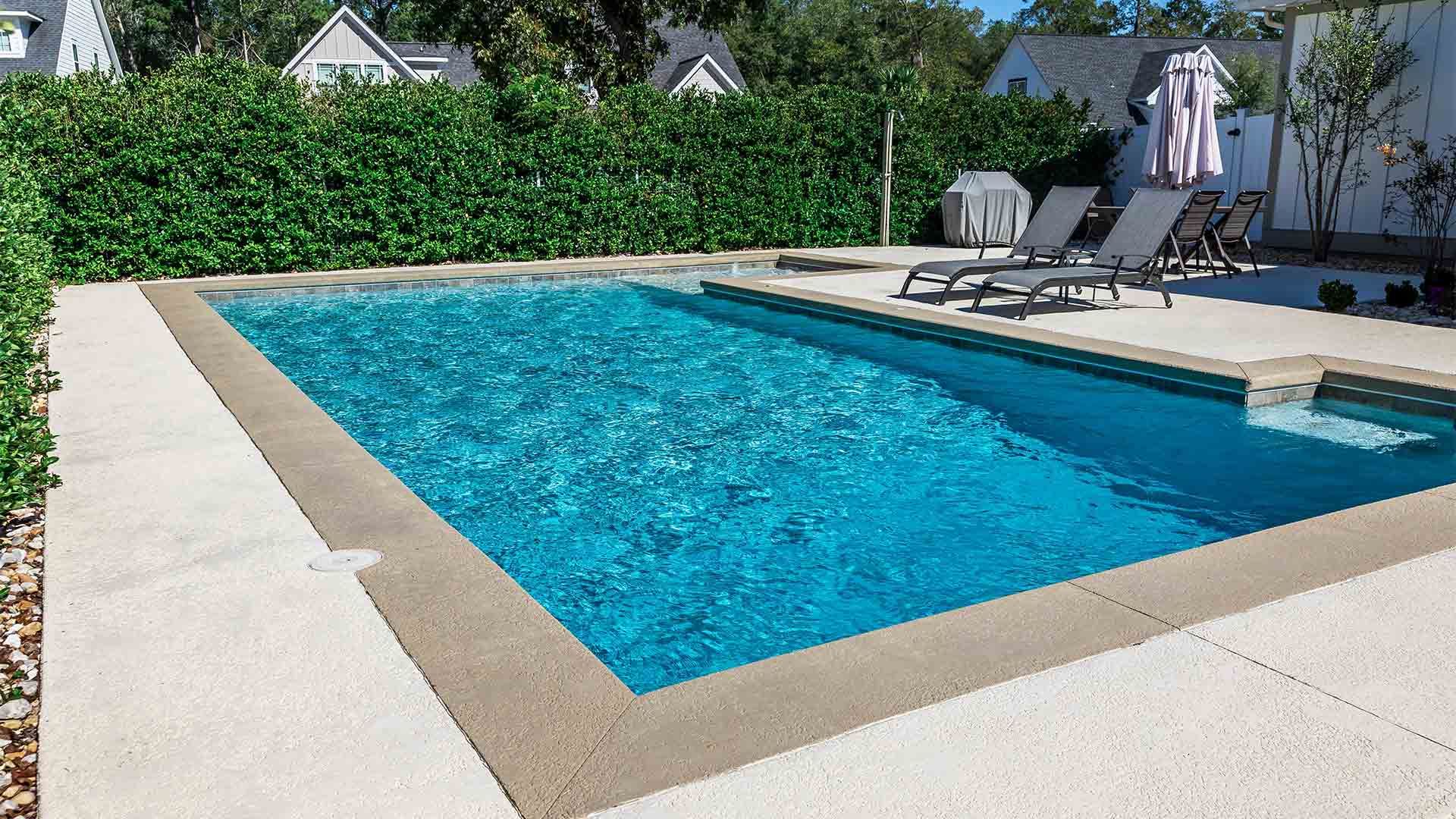 A large swimming pool surrounded by chairs and umbrellas in a backyard.