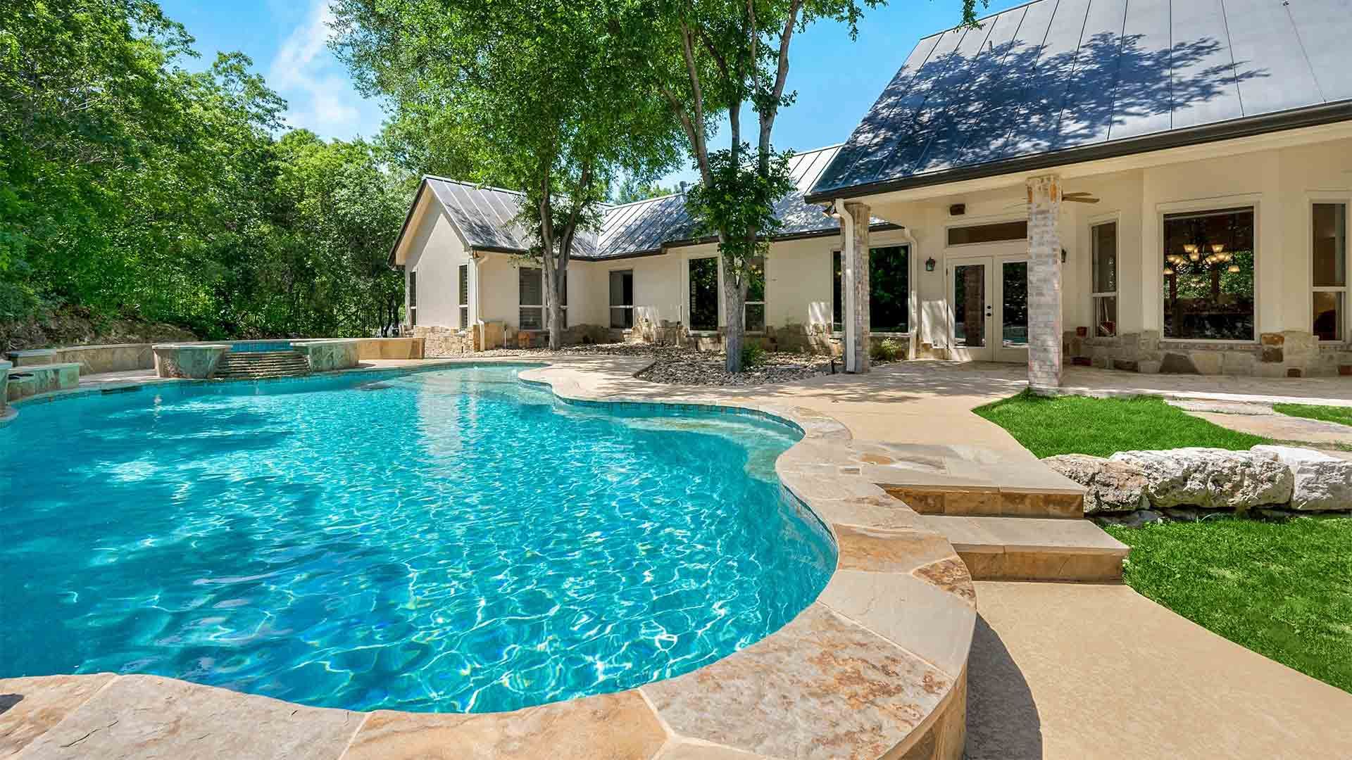A large swimming pool is in the backyard of a house.