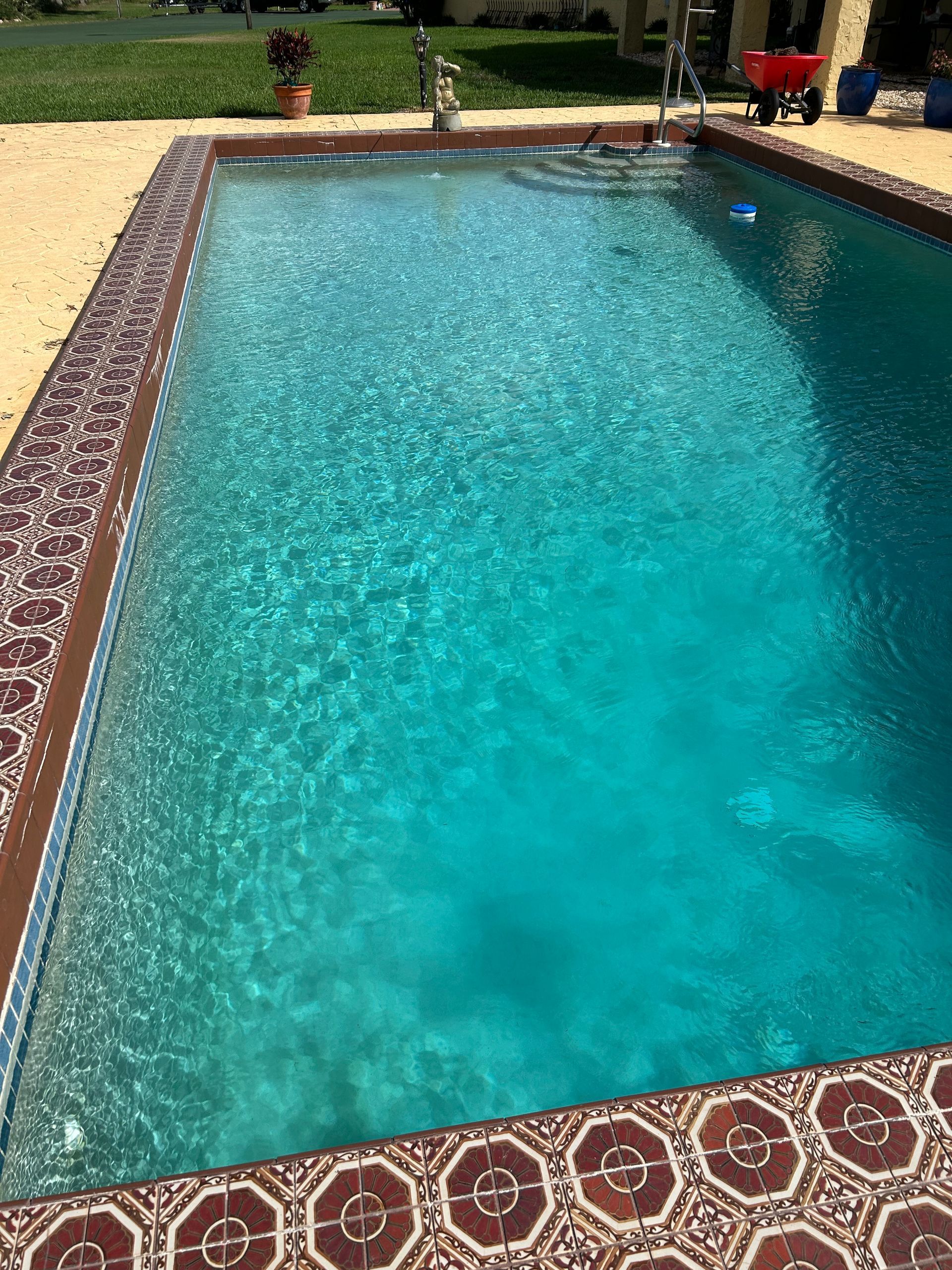 A large swimming pool with a red wheelbarrow in the background.