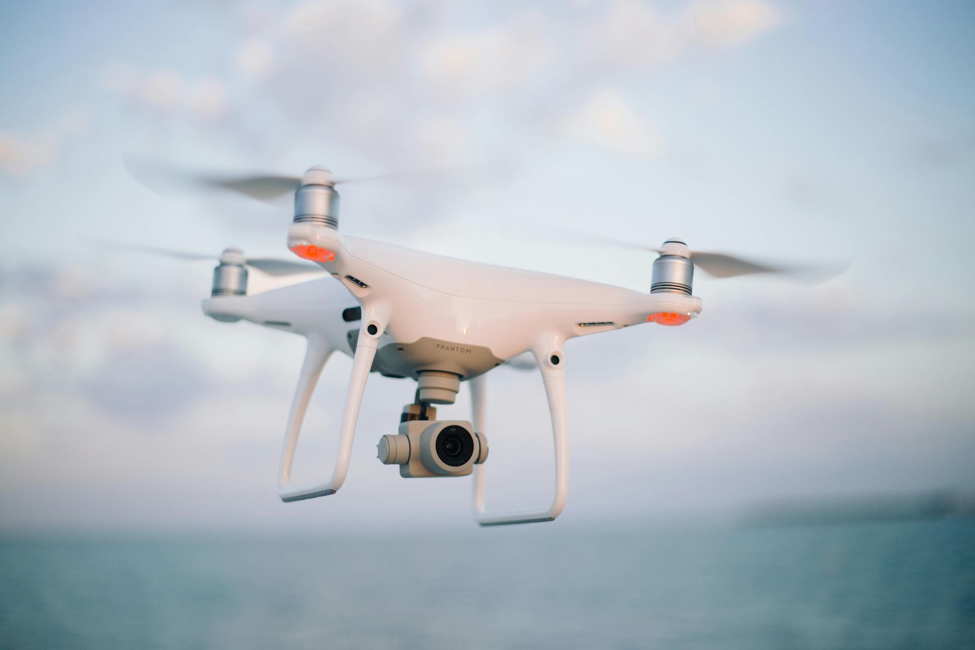 White quadcopter drone flying over the ocean at sunset, with a camera mounted underneath