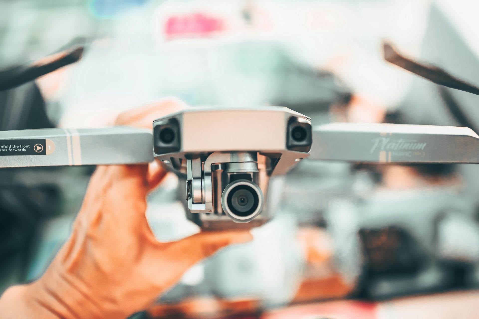 Close-up of a drone being held by hands, with propellers and camera visible against a blurred background