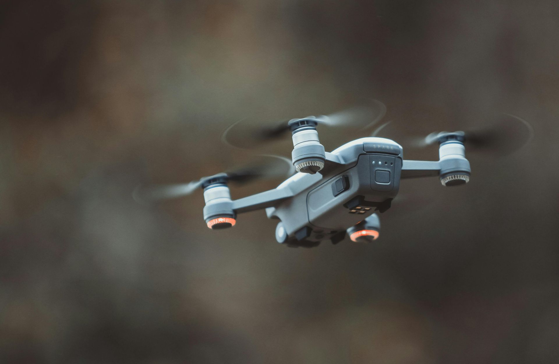 Gray quadcopter drone flying against a blurred brown background