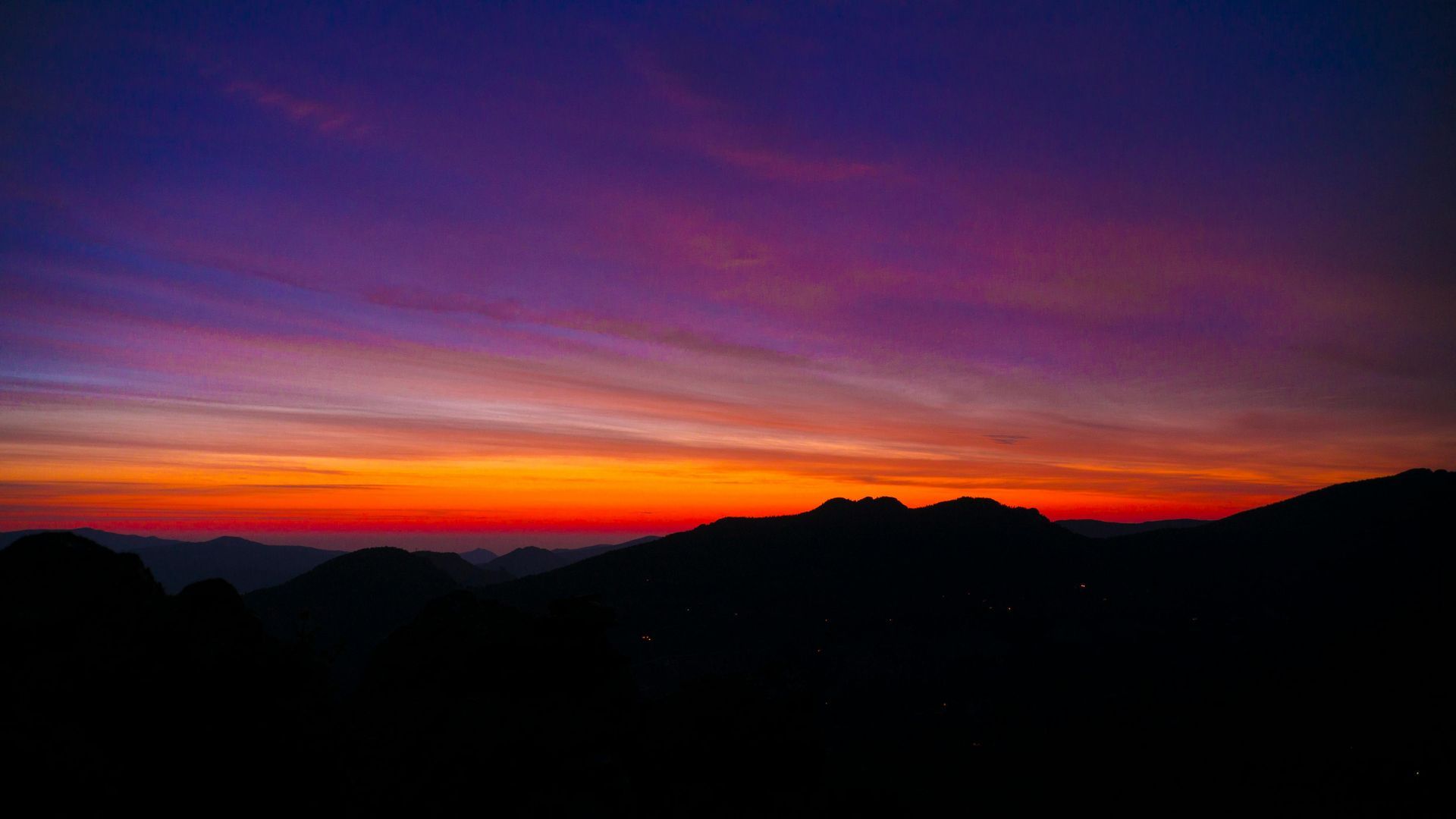Sunset over dark mountain range with vibrant orange and purple sky.